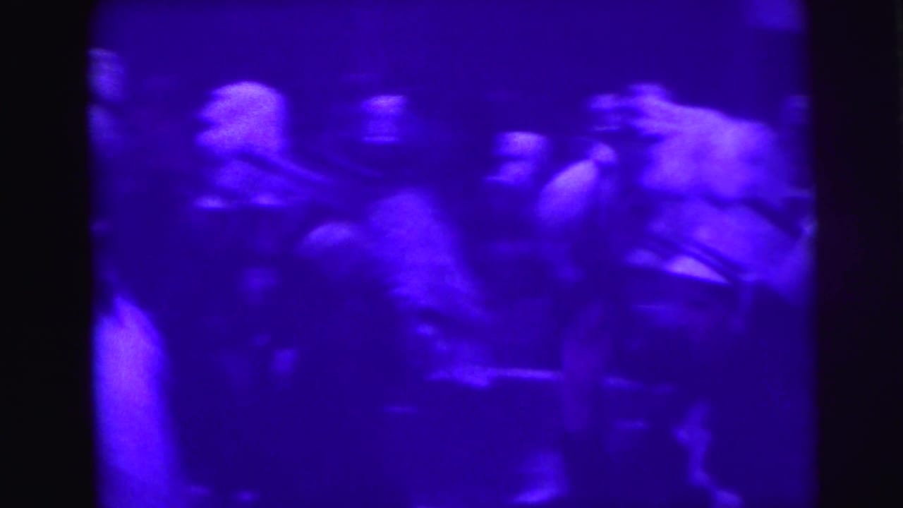 Blurred parade participants in uniforms move through a purple-tinted 8mm frame.