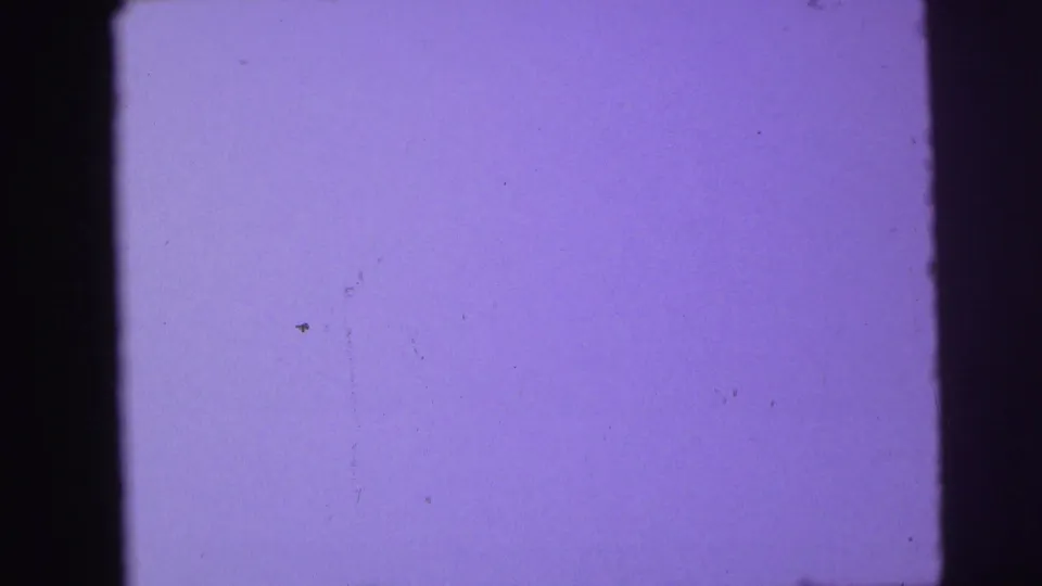 Purple-tinted exposed film frame with no clear subject, showing dust marks, scratches, and the black edge of the 8mm frame.