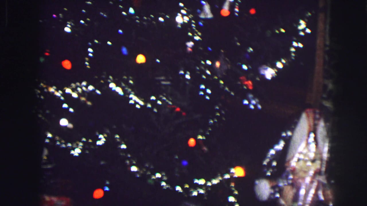 Close view of a dark Christmas tree with tinsel and multicolor lights.