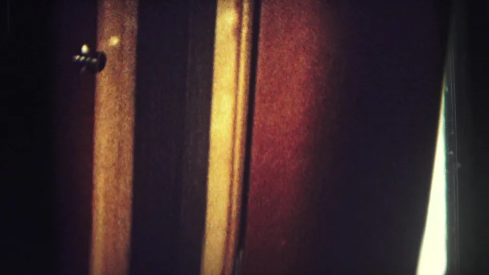 Grainy 8mm view of wood-paneled interior surfaces, with amber trim, reddish panels, and small hardware visible.