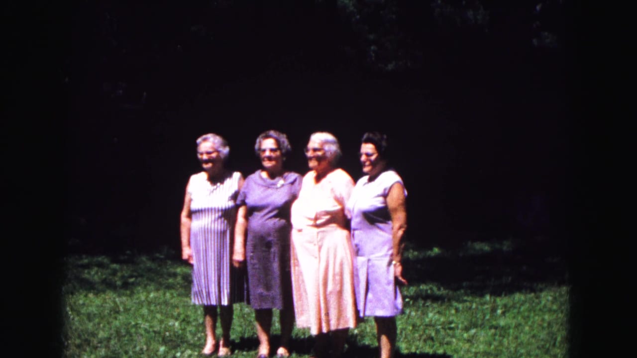 Four women continue posing together on grass, framed against a shaded background.