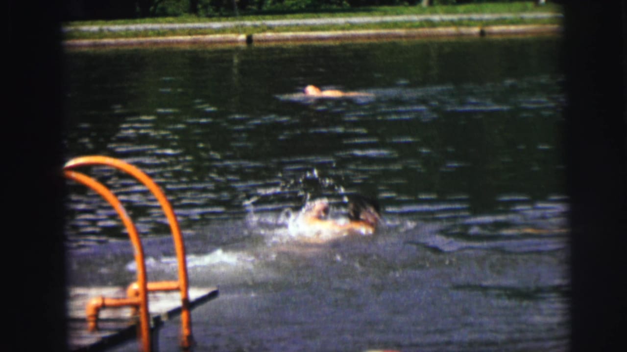 Swimmer surfaces with splashing water near a pool ladder.