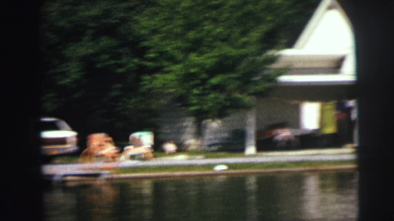 Waterside structure, parked station wagon, lawn chairs, and people near a reflective shoreline.