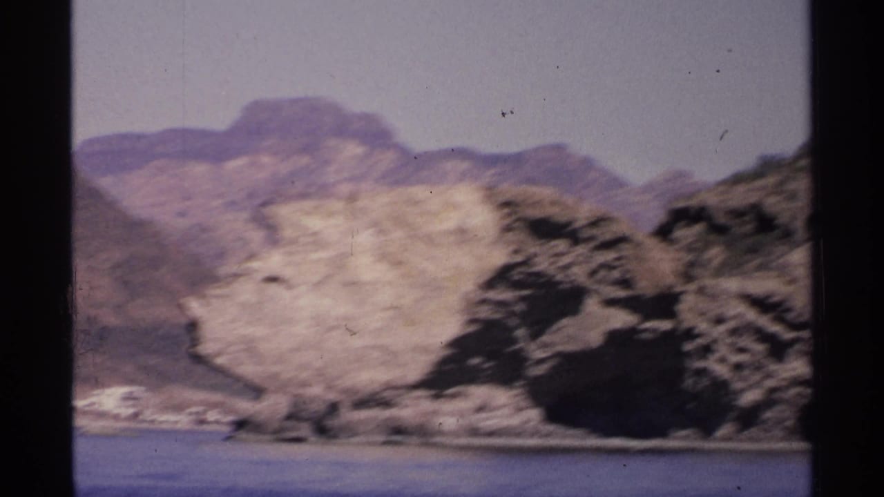 Rocky coastal cliff and blue bay with hazy mountains in the background.