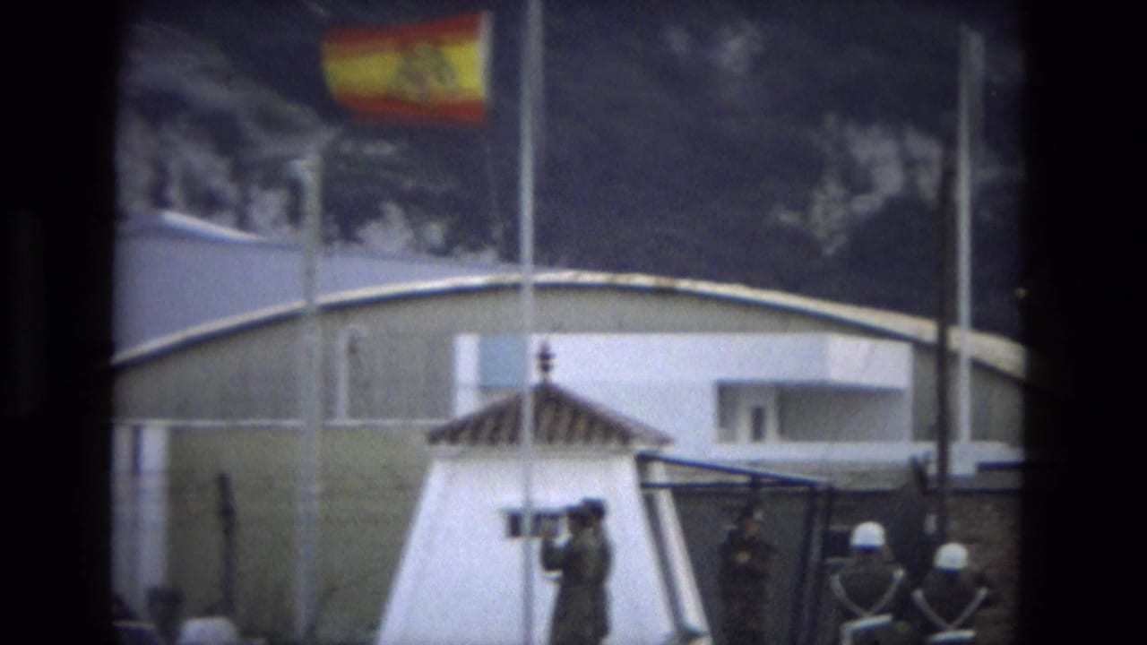 1978 Andalusia home-movie frame showing a Spanish flag, white sentry post, and uniformed soldiers during a formal ceremony.