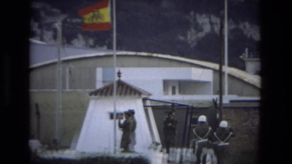 A distant 1978 Andalusia frame shows helmeted soldiers at attention beside a white sentry post and Spanish flag.