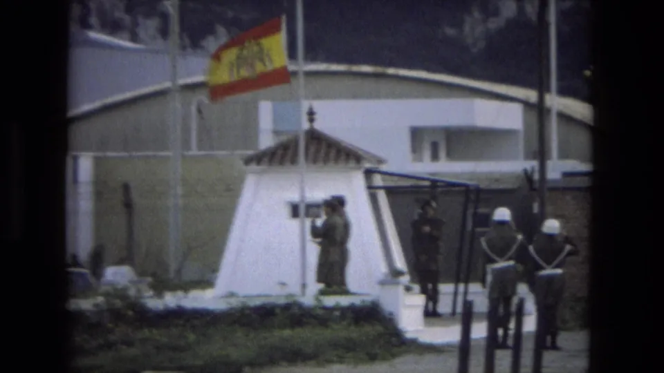 Late-1970s 8mm frame from Andalusia showing soldiers at a guard post during a Spanish flag-lowering ceremony.