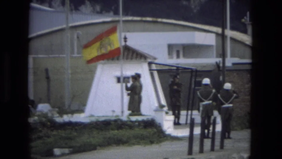1978 Andalusia frame with the Spanish flag at a guard post, uniformed soldiers in formation, and a gated area behind them.