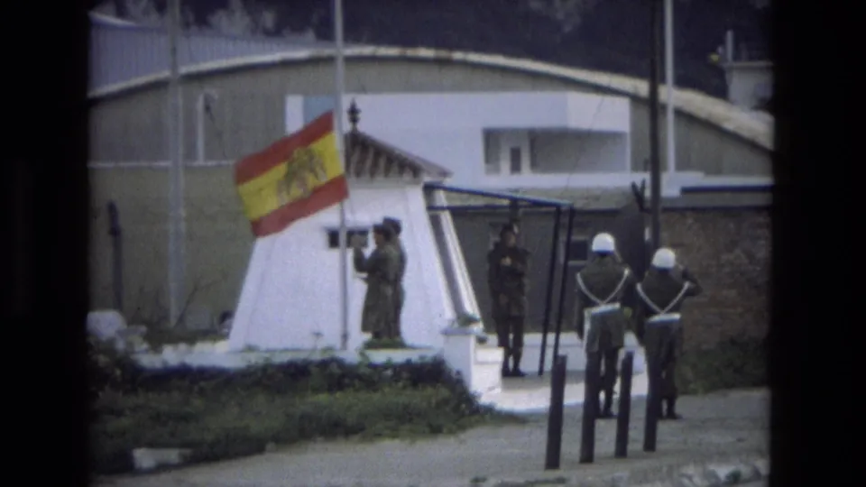 1978 Andalusia 8mm frame showing a soldier at the flag line and two helmeted guards standing with their backs toward the camera.