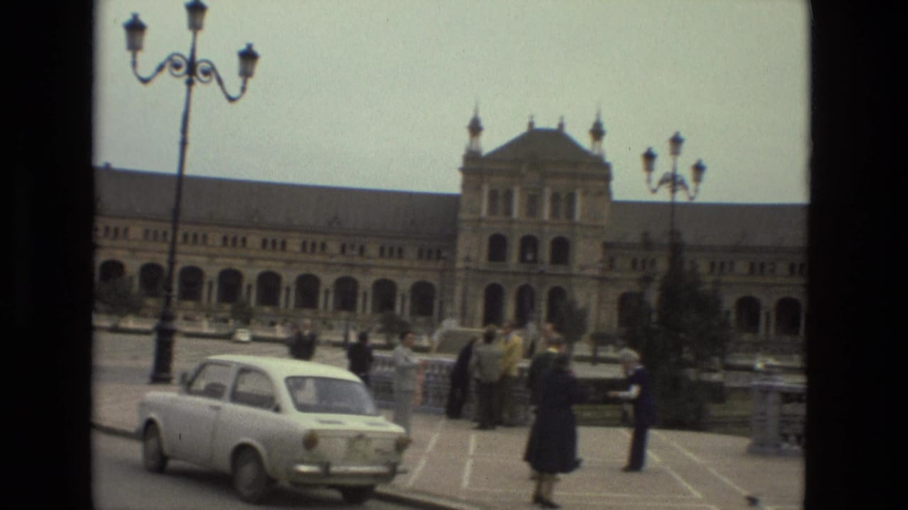 Historic arched building behind pedestrians and a white compact car in a public square.