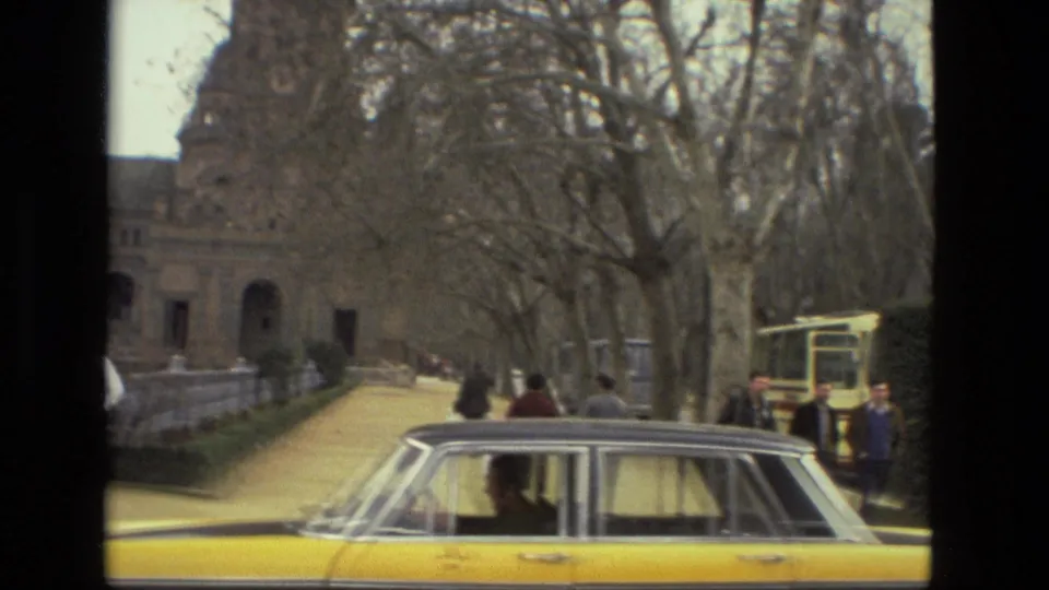 1978 Andalusia street view with a yellow taxi, pedestrians, tree-lined walkway, kiosk-like structure, and historic building entrance.