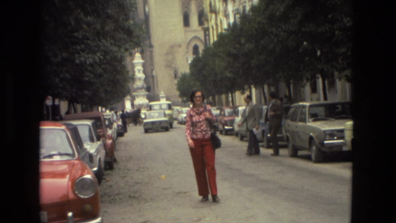 Woman in red pants standing in a tree-lined street with parked cars.