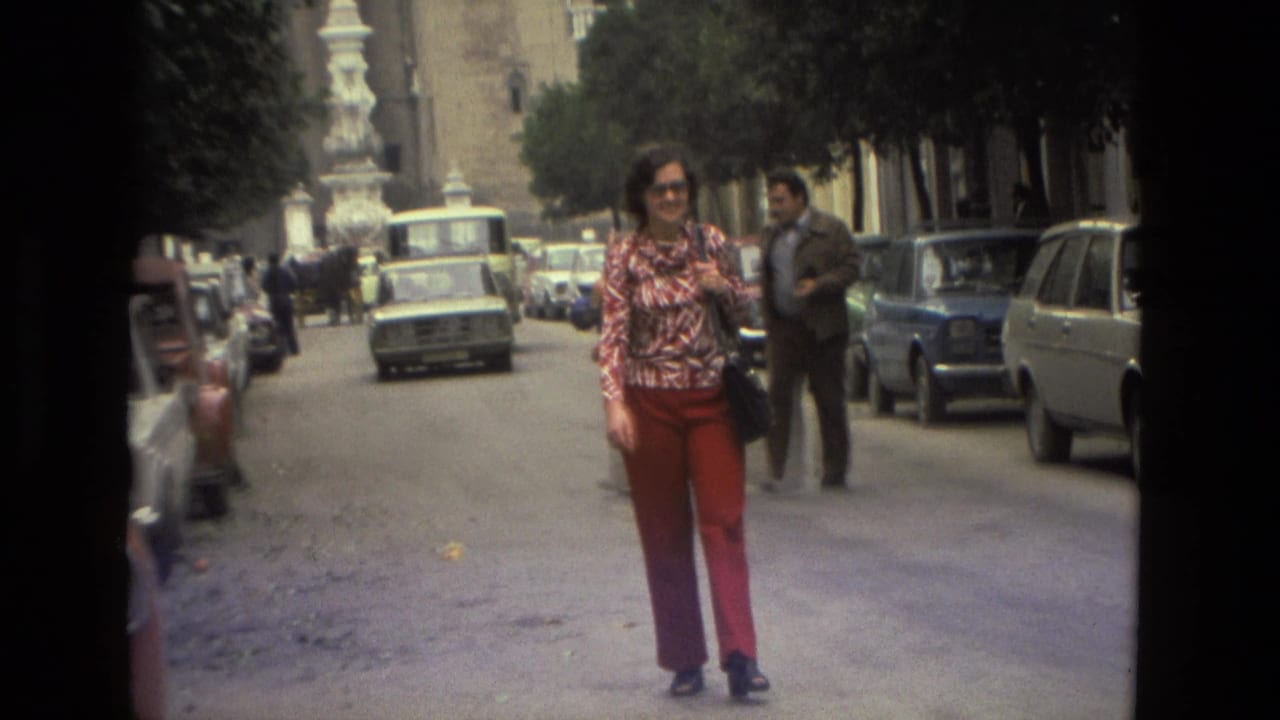 Woman walking toward the camera on a street lined with cars and trees.