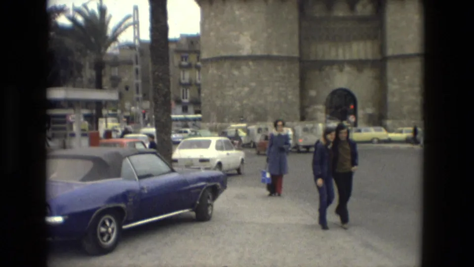 A blue classic convertible, pedestrians, palm trees, and a large stone tower appear in a 1978 Andalusia street scene.