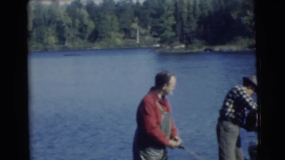 Two adult men continue fishing on a wooded Traverse City lake, with soft 8mm color and slight motion blur.