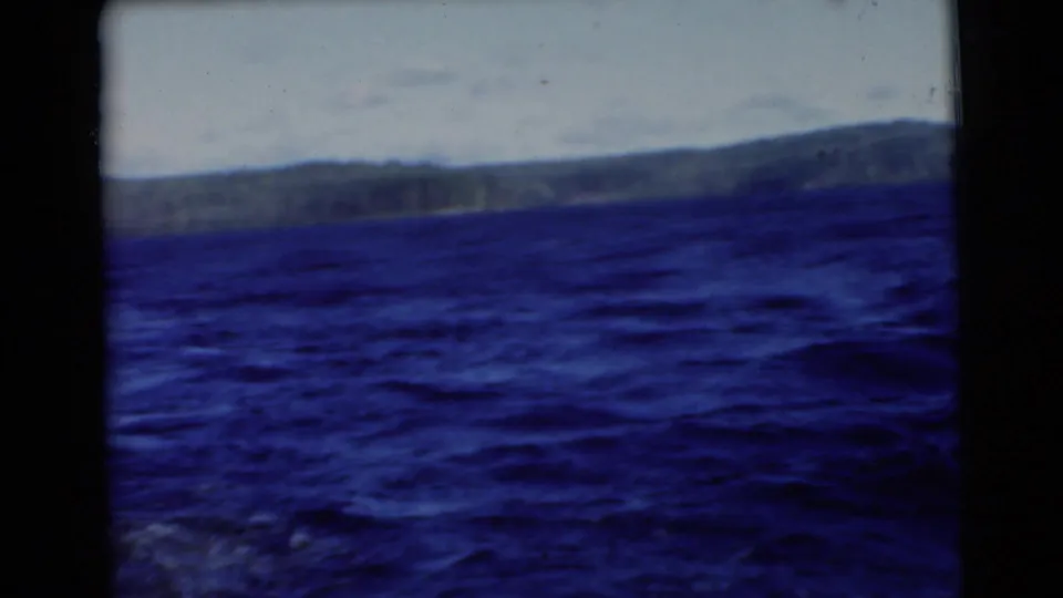Handheld 8mm frame of dark blue lake water and a soft distant shoreline, consistent with 1956 Traverse City footage.