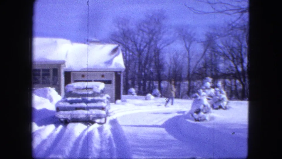 1963 Duluth frame showing a snow-covered driveway, parked car, garage, and a person with a small dog in the yard.