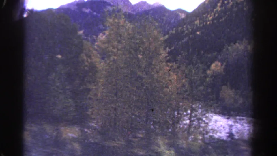 Archival 8mm view from above a mountain river, with dense trees, autumn color and dark ridgelines in the distance.