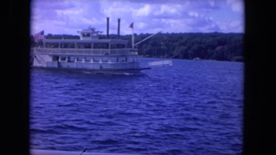 1972 Chicago-area lake scene with a white paddlewheel-style excursion boat near the frame edge, seen through dark 8mm film borders.