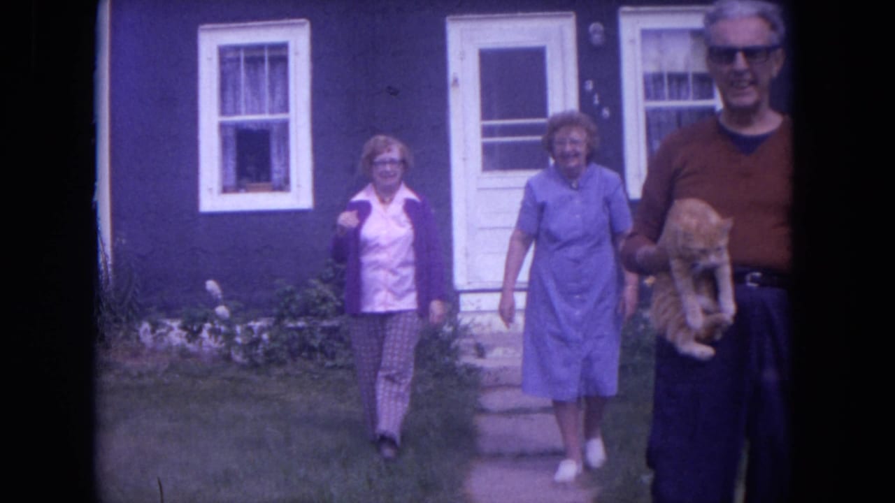 Three adults walk from a dark blue house while a man holds an orange cat.