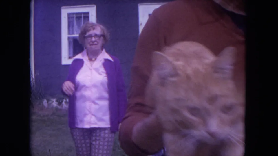 The orange tabby is brought close to the lens, partially obscuring the man, while a woman stands behind in the Chicago yard.