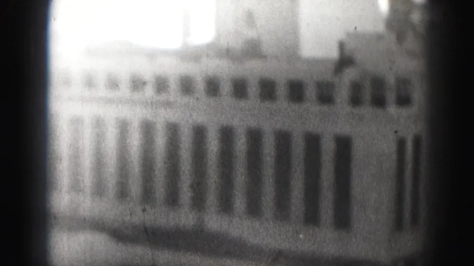 Black-and-white 8mm view of a Harrisburg urban building, with tall window bays, bright sky, grain, and soft focus.