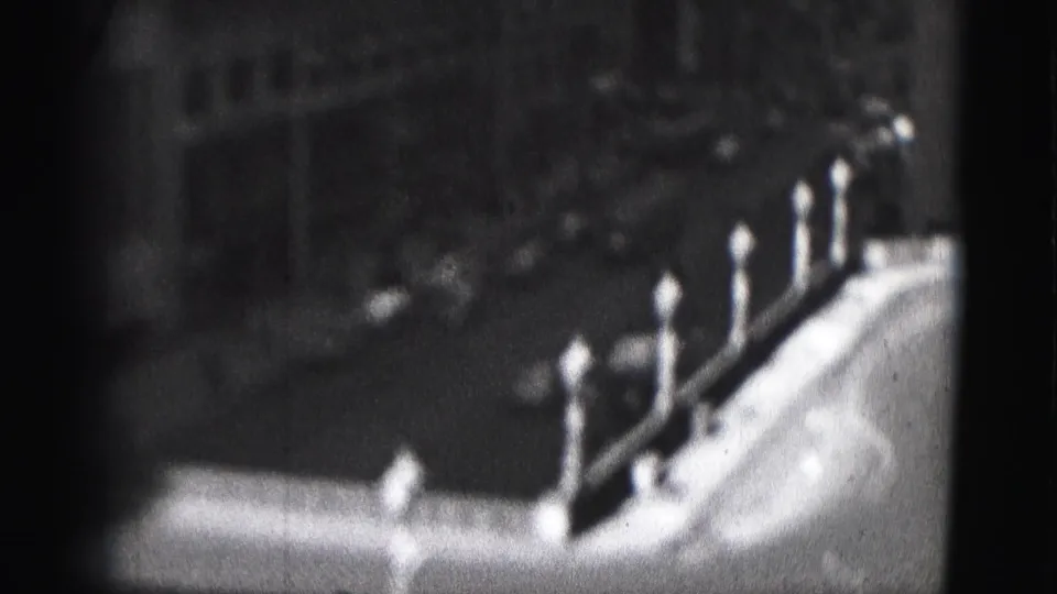 1946 Harrisburg 8mm frame showing globe lampposts along a bright edge with shadowed urban forms beyond.