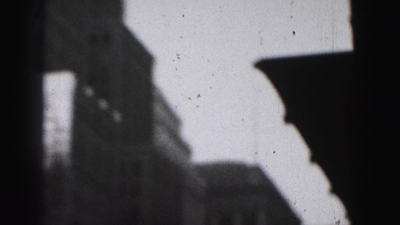 Dark high-rise silhouettes against a bright sky in a grainy 8mm frame.