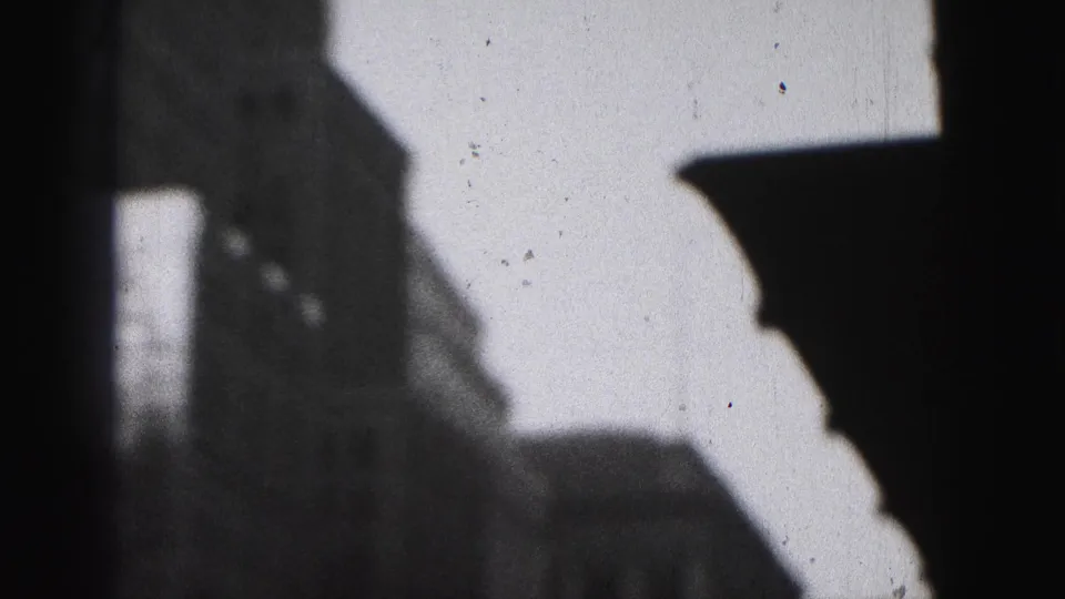 1946 Harrisburg home-movie frame showing shadowed tall buildings and a bright sky with visible film grain and edge marks.