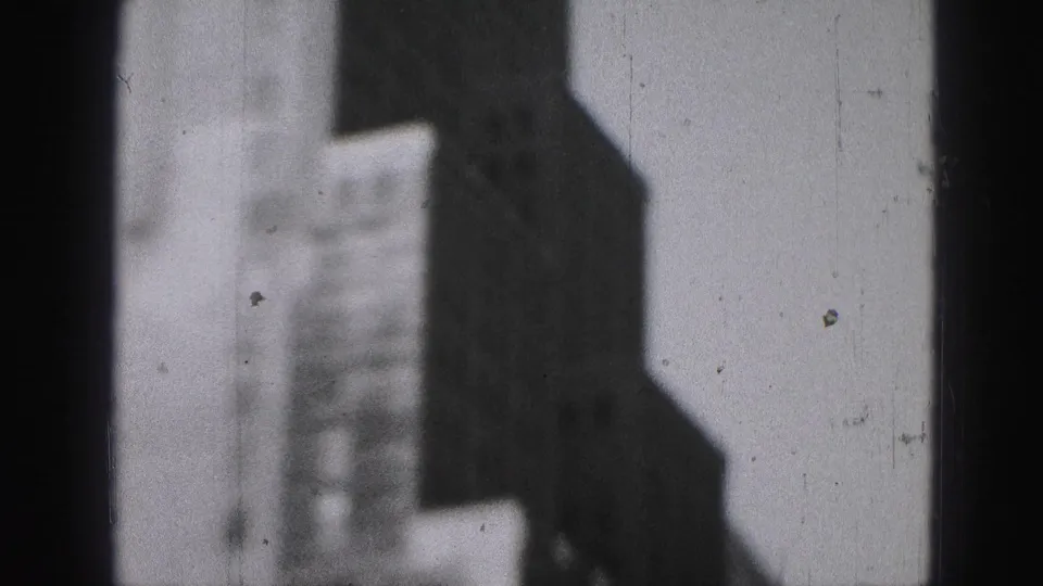 1946 Harrisburg frame with dark vertical building masses, a pale distant facade, and visible scratches from the 8mm source.