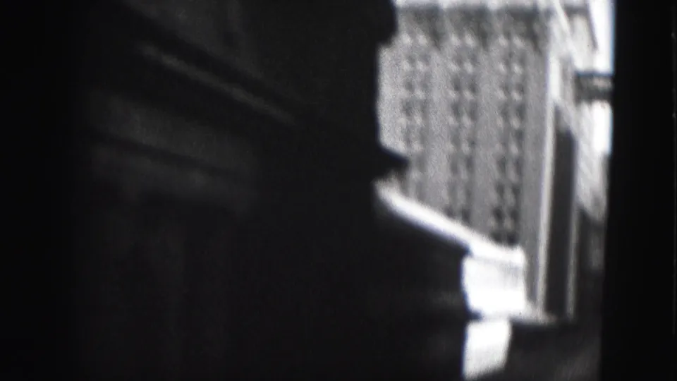High-contrast 8mm frame from Harrisburg showing a dark building edge and a brighter windowed structure beyond it.