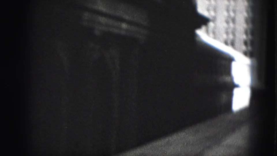 Shadow-heavy 1946 Harrisburg frame looking along a dark building wall toward a brighter facade and narrow passage of light.