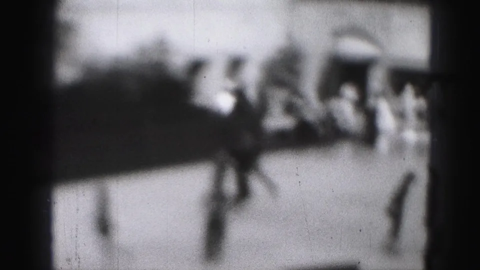Hazy 8mm frame from the Harrisburg skating scene showing a dark moving figure and indistinct rinkside crowd.