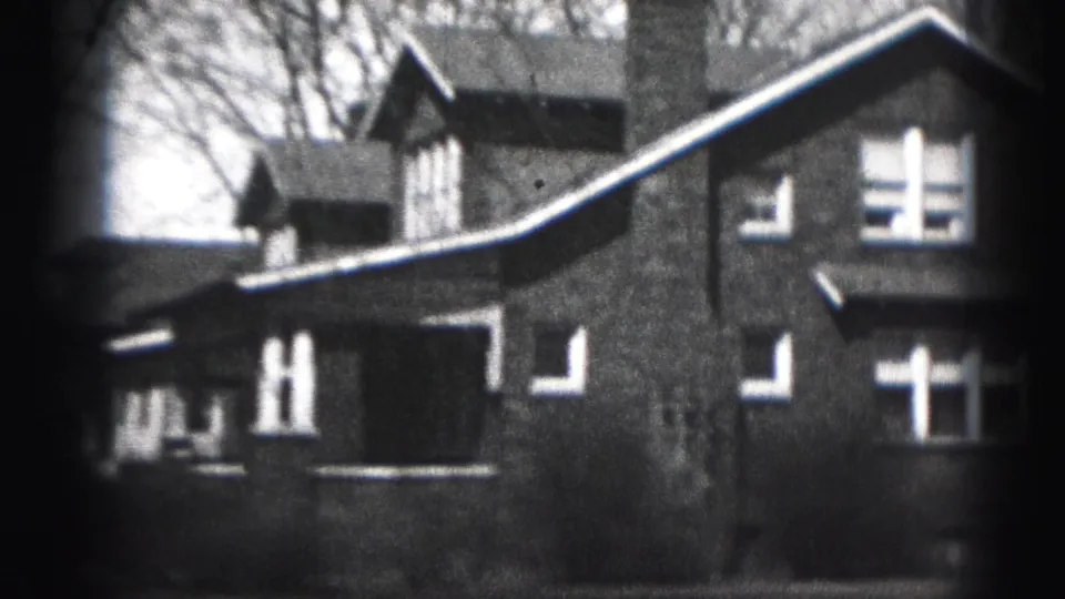 Black-and-white 8mm view of Harrisburg houses with steep rooflines, chimney, light window trim, and bare trees.