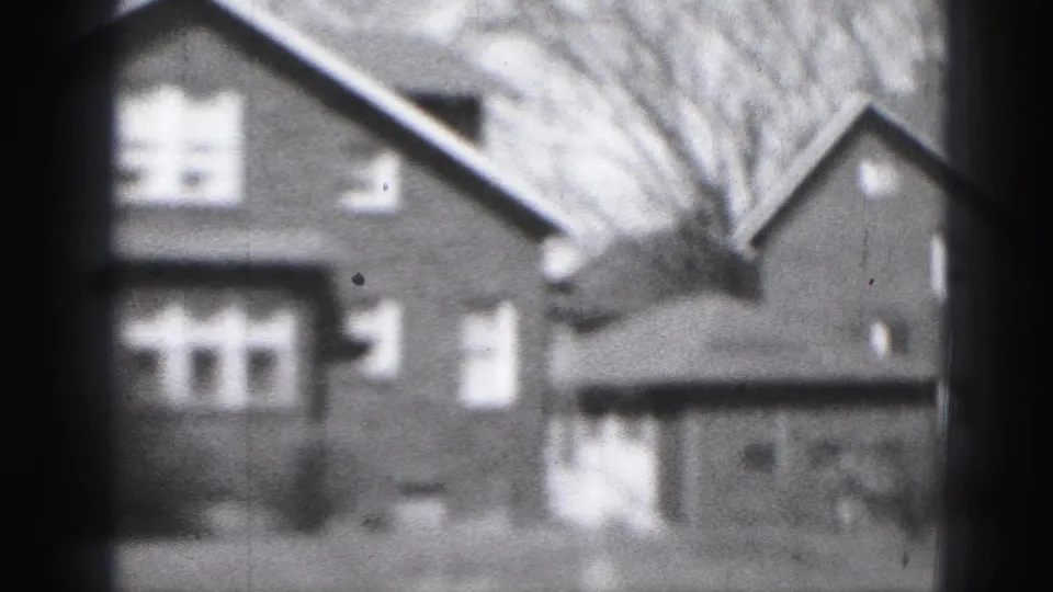 Soft-focus 1946 Harrisburg home-movie frame with brick residential buildings, a garage, and leafless trees.