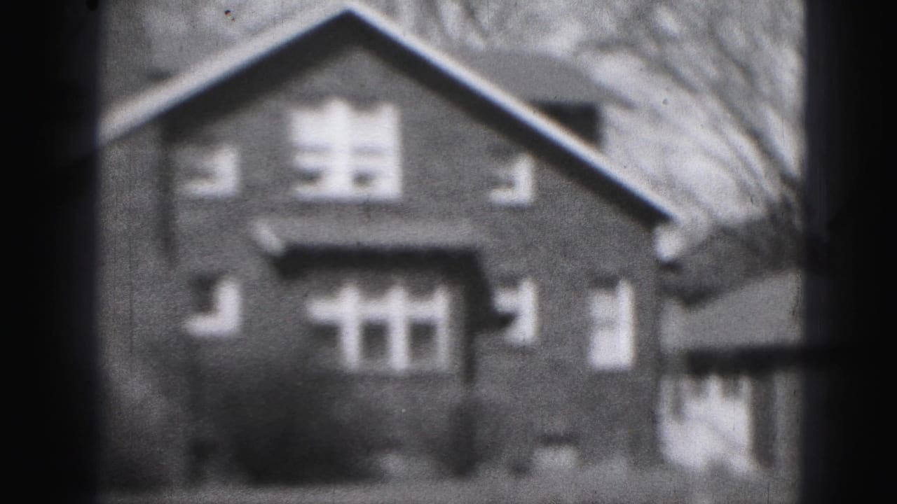 Soft black-and-white view of a gabled two-story house seen from outside.