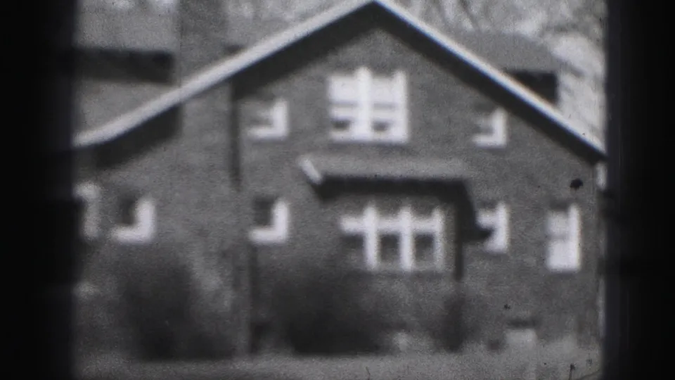 Soft 1946 home-movie frame of a Harrisburg house exterior, with symmetrical windows, shrubs, and dark vignetting at the edges.