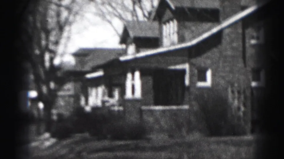 1946 Harrisburg home-movie frame showing a brick residential house from the street with bare trees and soft 8mm focus.