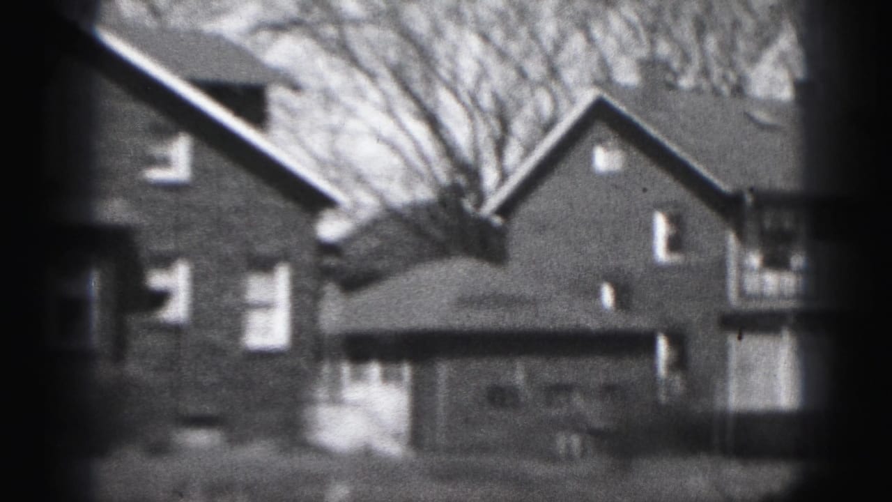 1946 Harrisburg home-movie frame showing brick houses, pitched roofs, windows, and bare trees in soft black-and-white film texture.