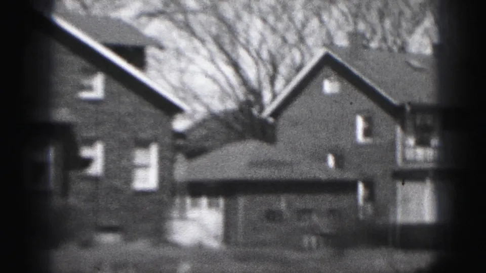 1946 Harrisburg home-movie frame showing brick houses, pitched roofs, windows, and bare trees in soft black-and-white film texture.