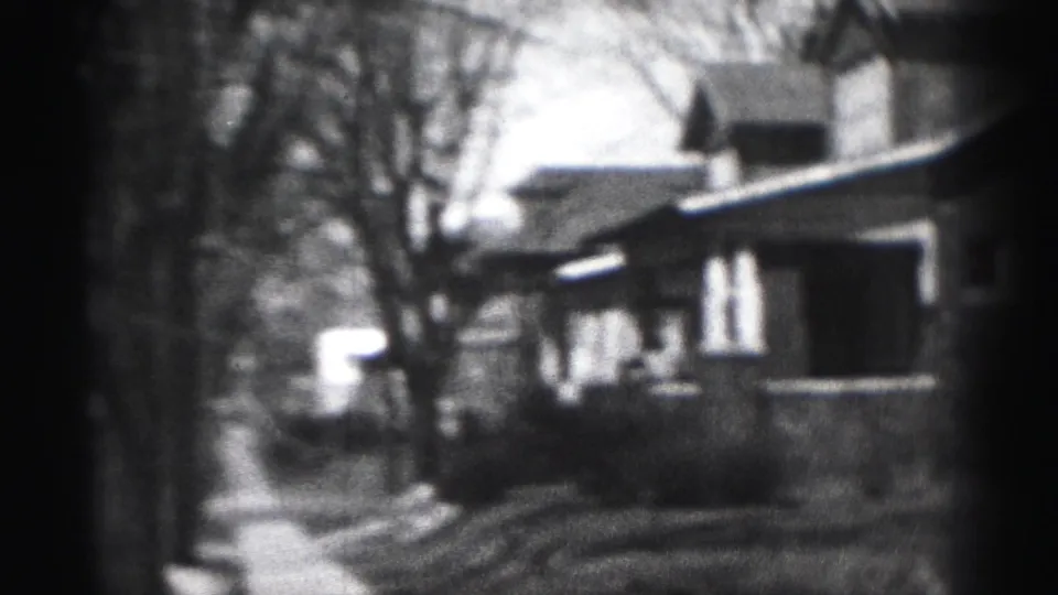 Soft 8mm frame showing a Harrisburg residential block with brick homes, porch shapes, bare trees, and a sidewalk or yard edge.