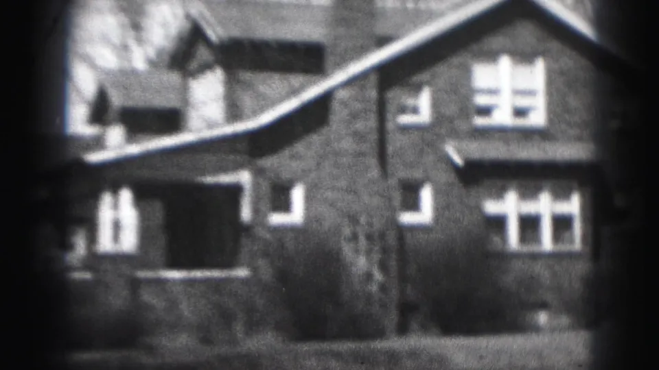 1946 Harrisburg home-movie frame with a brick house facade, multi-pane windows, roofline, shrubs, and soft film exposure falloff.