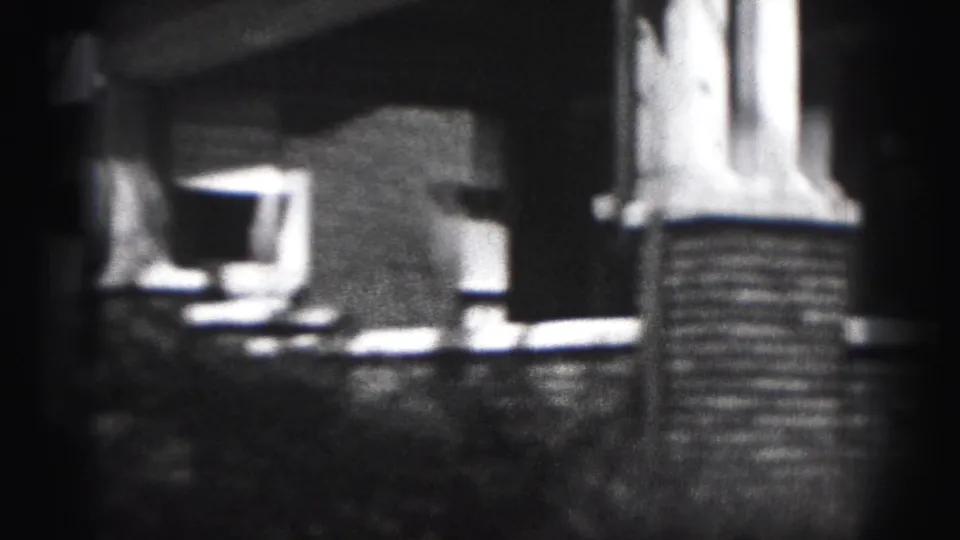 Side-angled 1946 home-movie frame of a Harrisburg brick house porch, with column, steps, low wall, and deep shadow around the entrance.