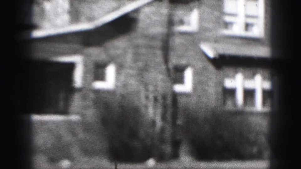 1946 Harrisburg home-movie frame showing a brick residential facade, windows, shrubs, and soft 8mm focus.