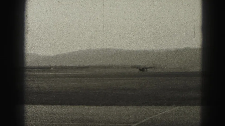 Small aircraft at the far side of the Harrisburg airfield, seen against a hazy 1940s runway landscape.