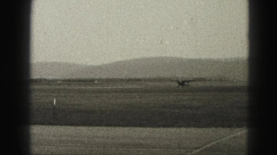 The small plane moves across the open Harrisburg-area runway, seen through dark 8mm gate borders and haze.