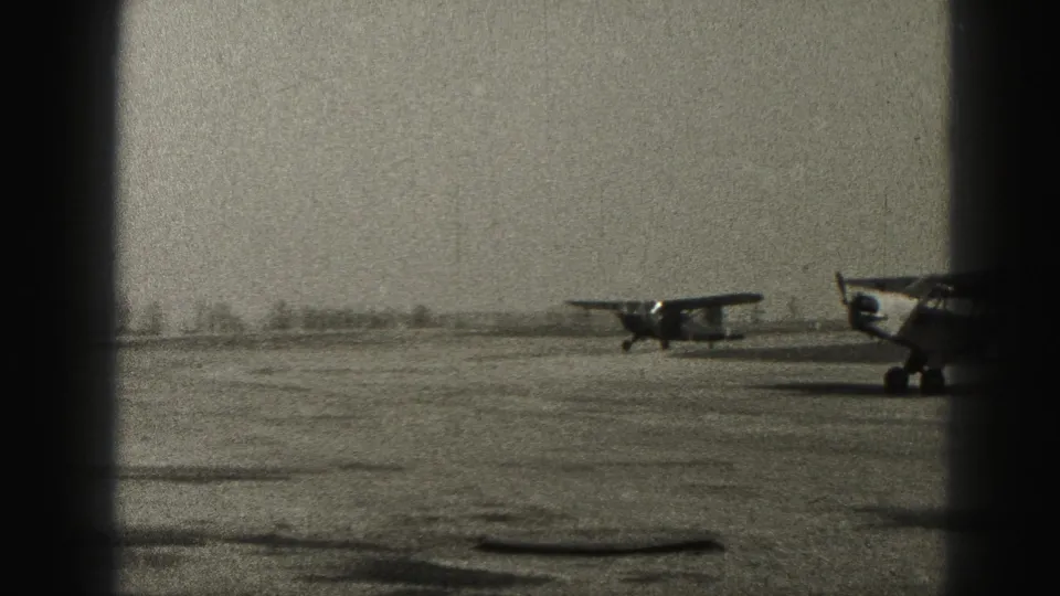 Two small propeller aircraft are visible on the Harrisburg runway, with the nearer plane partly cropped by the film frame.
