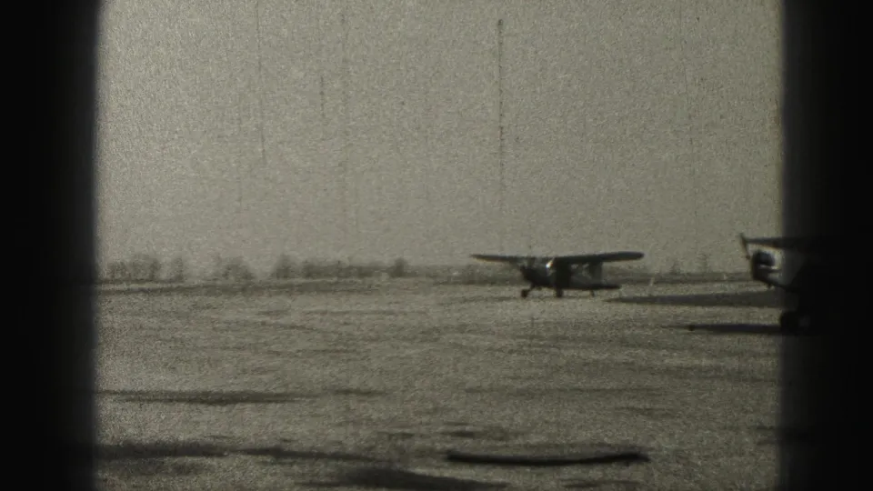 A small propeller aircraft taxis on a Harrisburg-area runway in 1946, seen through dark vertical framing on black-and-white 8mm film.