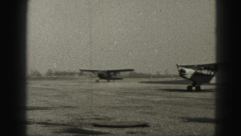 The taxiing propeller plane passes across the runway while another aircraft is partly visible at the right side of the 1946 Harrisburg footage.