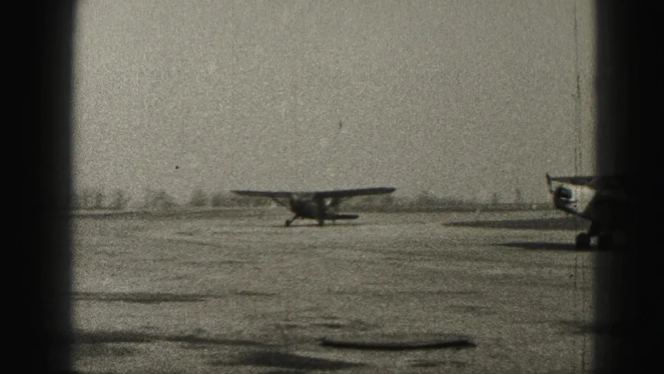 A small aircraft moves across the airfield while a second plane remains partly in frame, captured in grainy 1946 Harrisburg home-movie footage.